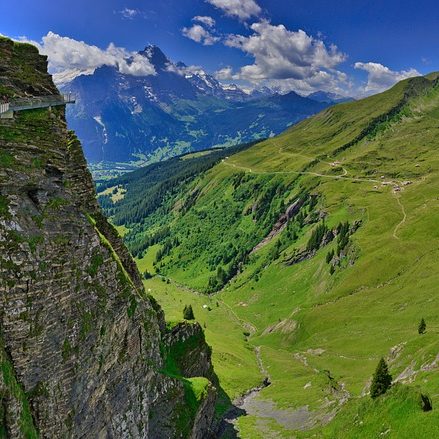 Blick auf grüne Täler und majestätische Berge unter einem blauen Himmel.