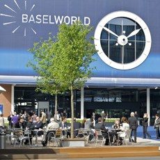 Besucher auf einer Terrasse vor einem großen Uhrenstand bei Baselworld.