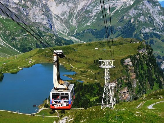 Seilbahn fährt über eine grüne Landschaft mit Berg und blauem See.