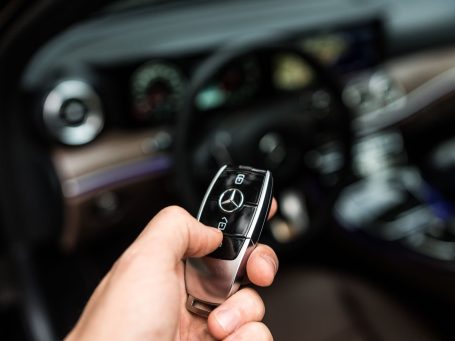 Hand hält einen Mercedes-Benz Schlüssel in einem Fahrzeuginterieur.