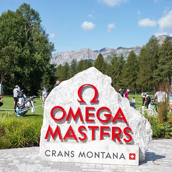 Stein mit dem Logo der Omega Masters in Crans Montana, umgeben von Natur und Menschen.