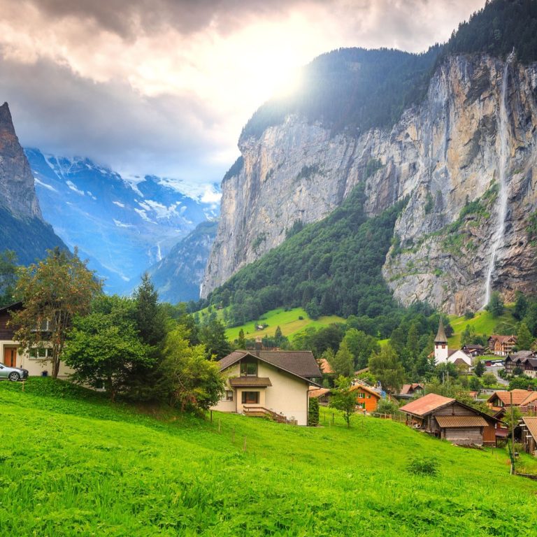 Berglandschaft mit Wasserfall, grünen Wiesen und traditionellen Chalets im Tal.