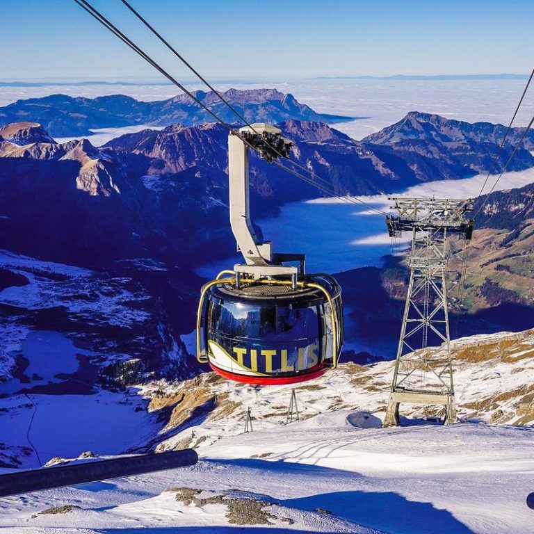 Gondelbahn fährt über schneebedeckte Berge mit Blick auf ein tiefes Tal.