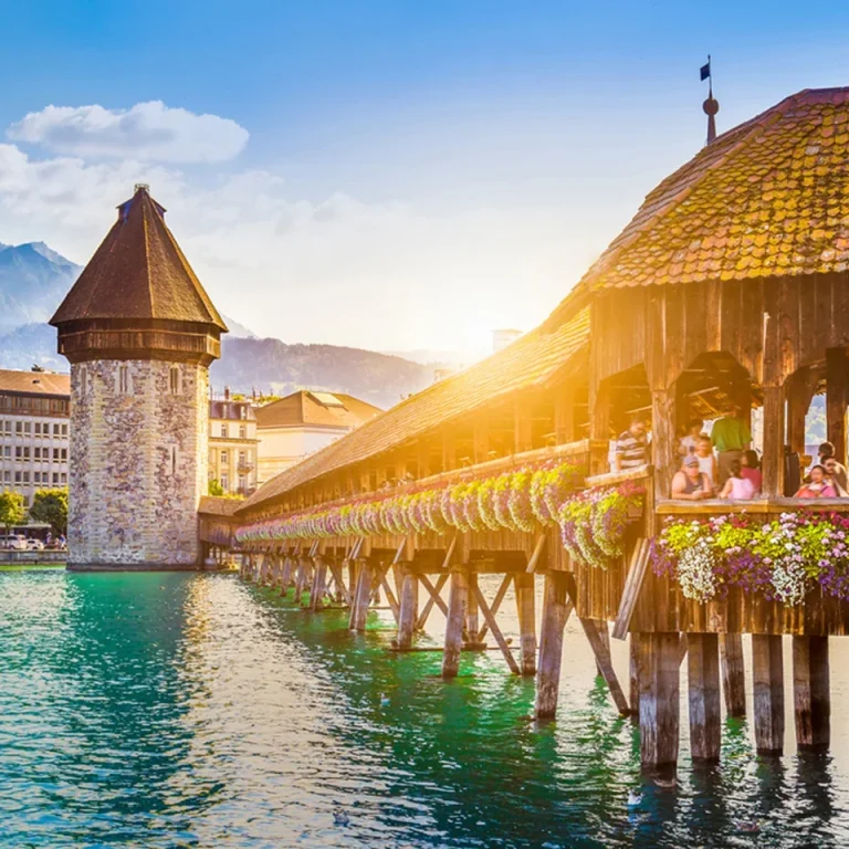 Kapellbrücke in Luzern mit historischem Wasserturm und blühenden Pflanzen am Ufer.